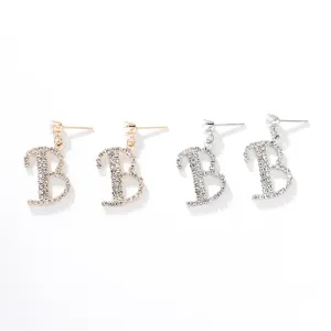Primo piano dettagliato di orecchini pendenti con lettera B in strass brillanti, oro e argento.