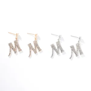 Primo piano di orecchini con lettera M in strass brillanti, dettagli in cristallo e perno in argento.