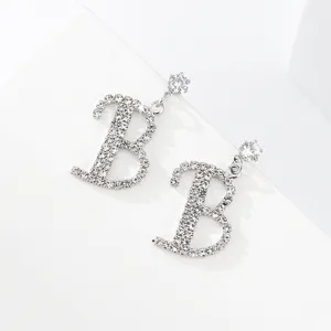 Dettaglio in primo piano di orecchini pendenti con lettera B in strass brillanti.