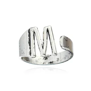 Gros plan de la bague ouverte lettre M en argent vintage avec une finition texturée.
