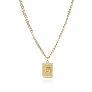Gold necklace detail featuring a rectangular pendant with engraved letter G and sunburst rays.