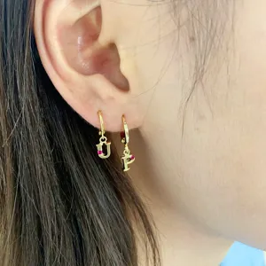 Gold letter hoop earrings with red stone accent, delicate initial huggie earrings detail.
