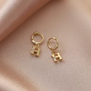 Gold letter H drop earrings with sparkling rhinestone detail, elegant jewelry detail shot.