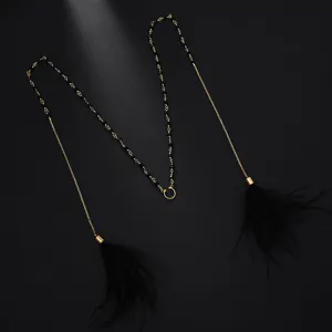 Detail view of bohemian feather face chain with gold metal links and black tassel charms.