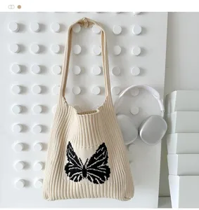 Detailed shot of knitted shoulder bag with black butterfly pattern on minimalist pegboard display.