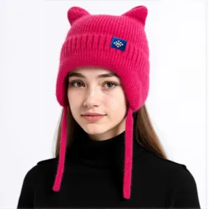 Nahaufnahme der rosa gestrickten Katzenohrenmütze mit Ohrenklappen und Schneeflockenetikett.