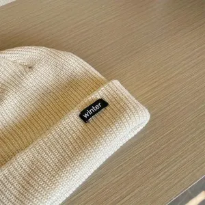 Close-up detail of the beige knitted winter beanie hat showing fine texture and knit weave.