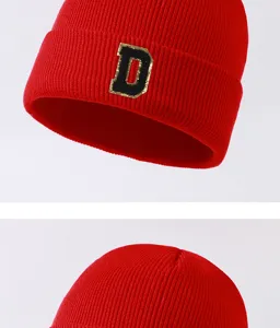 Red knit beanie hat detail view featuring a stylish black and gold letter D patch for winter.