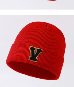 Close-up detail of a red knitted beanie featuring a stylish black and gold letter V patch.