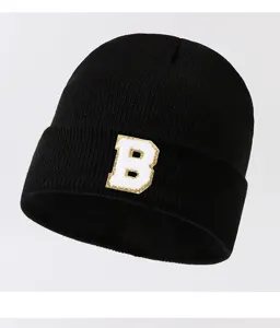 Close up of a black knit beanie hat featuring a stylish white letter B patch on the cuff.