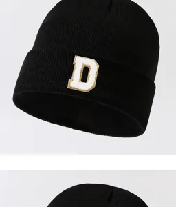 Close-up of black knitted beanie hat featuring a stylish textured letter patch detail for street fashion.