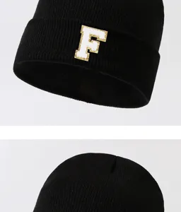 Close-up of black knitted beanie featuring a white letter F patch with gold glitter edge.