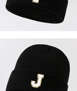 Detail view of black knit beanie hat with white and gold letter J patch embroidery.