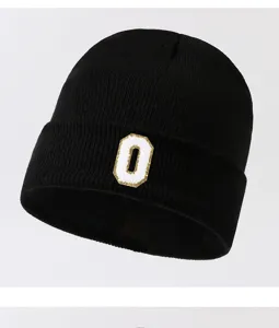 Close-up detail of black knitted beanie hat featuring white and gold letter O patch