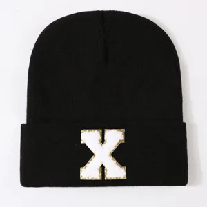 Black knit beanie hat with white gold letter X patch front view isolated product main image.