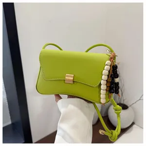 Dettaglio borsa tracolla minimal verde, finitura pelle con ciondolo di perline in legno.