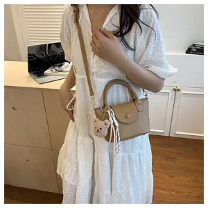 Detail view of a stylish textured crossbody bag with a cute bear pendant and chic ribbon charm.