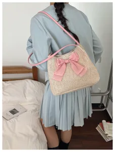 Detail view of stylish straw tote bag with pink bow and shoulder strap in casual indoor setting.