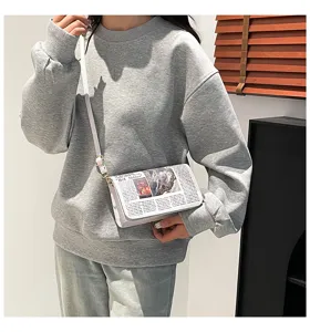 Vue rapprochée détaillée d'un sac à bandoulière blanc pour femme avec imprimé journal.