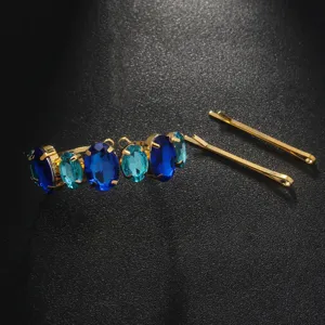 Close-up detail shot of crystal rhinestone hair clip and bobby pins in blue and gold tones.