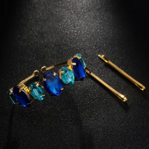 Close-up of elegant rhinestone hair hoop with deep blue crystals and matching gold bobby pins.