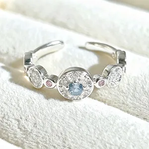 Detailed close-up of a sweet open silver ring featuring a sparkling light blue center stone.
