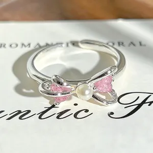 Close-up of a silver open ring featuring a bow design with pink cubic zirconia and a pearl.