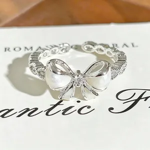 Close-up of exquisite silver bow ring with white enamel and sparkling zircon details.