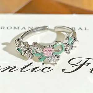 Detailed view of silver open ring showing pink zircon and green enamel bow with sparkling stones.
