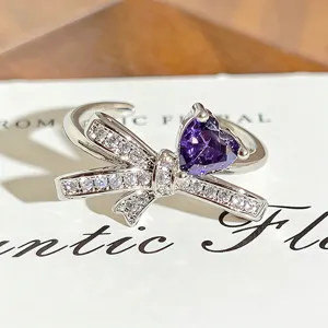 Close-up detail of silver bow open ring featuring sparkling white zircons and purple heart stone.