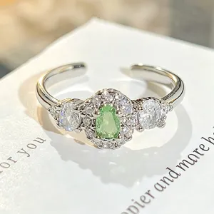 Primer plano detallado de anillo abierto de plata con circonita verde clara y piedras.