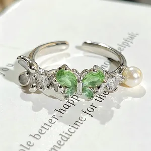 Detalle de primer plano del anillo abierto de cristal de mariposa verde con circón y perla.