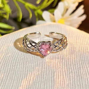 Detailed close-up of a silver open ring with a sparkling pink heart zirconia and delicate wing details.