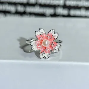 Close-up of enamel cherry blossom ring with pearl center, adjustable open band design.