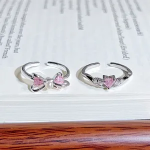 Close up detail of dainty silver open rings with sparkling pink zircon bow and heart design.