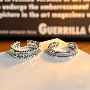 Detailopname van zilveren open ringen met blauwe vierkante zirkonia en fijne textuur.