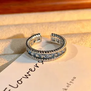 Open zilverkleurige ring met een rij vierkante blauwe zirkonia's en gedraaide touwmetaalranden.