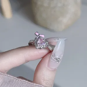 Nahaufnahme eines verspielten silbernen offenen Rings mit rosa Zirkonherz und Schleife.