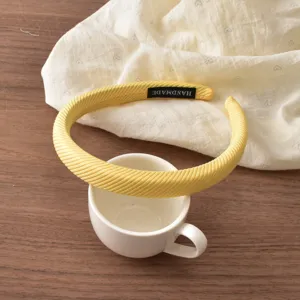 Close-up detail of yellow diagonal stripe sponge headband with handmade tag on wooden table.