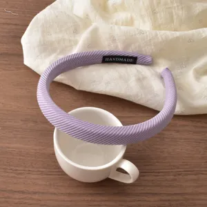Detailed view of a purple diagonal striped headband featuring a handmade fabric tag on wood.