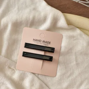 Minimalistische schwarze Acetat-Haarspangen auf rosa Karte, elegantes Haaraccessoire Alltag.