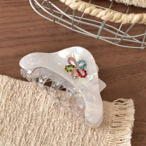 Primo piano di molletta per capelli perlata lucida decorata con trifogli in strass colorati.