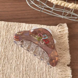 Primo piano del fermaglio per capelli in resina marrone con dettagli di fiori in strass colorati.