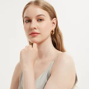Close-up detail view of minimalist thick gold hoop earrings worn by model in studio shot