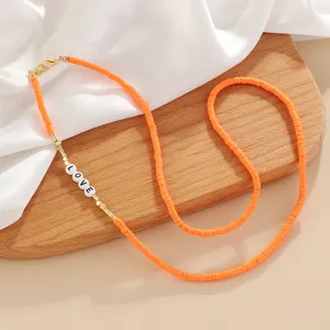 Detailed close-up of orange heishi disc bead necklace with LOVE letter beads and gold accents.