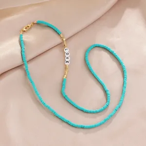 Turquoise heishi bead necklace detail featuring gold metal accents and white LOVE beads.