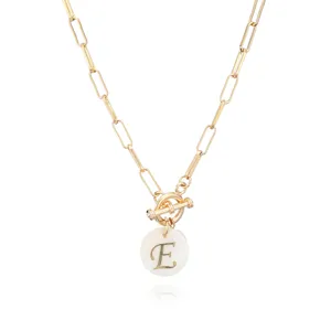 Detailaufnahme einer goldenen Büroklammer-Halskette mit weißem Muschel-Buchstaben-E-Anhänger.