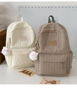 Vue détaillée de sacs à dos plissés élégants en crème et kaki avec des pompons en peluche.