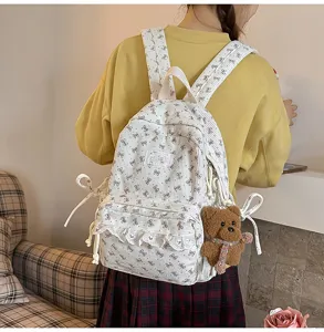 Detail view of white corduroy backpack with bow print, lace trim and cute bear pendant.