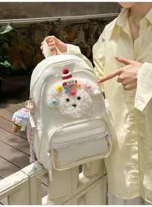 Vue détaillée du sac à dos blanc avec peluche chiot, bordure en dentelle et pompons colorés.